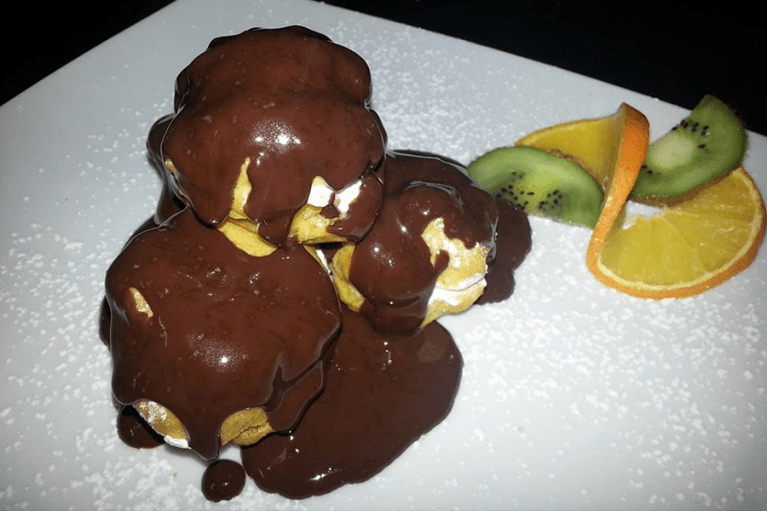Profiteroles al cioccolato con fette di kiwi e arancia.