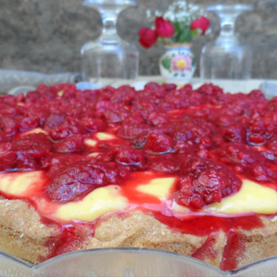 Crostata con crema e lamponi su piatto trasparente.