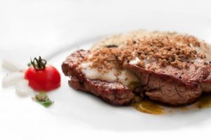 Bistecca con formaggio e pomodoro su piatto bianco.