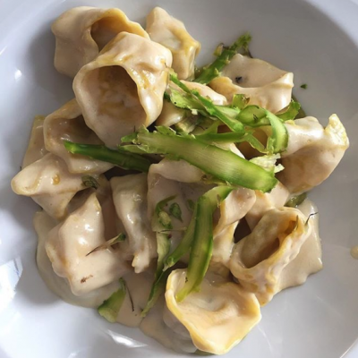 Tortellini con crema e asparagi su piatto bianco.