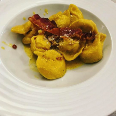 Tortellini con pancetta e formaggio su piatto bianco.