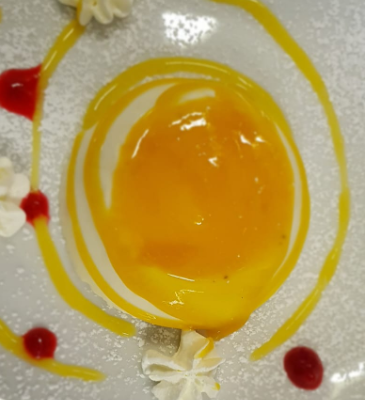 Dessert con crema gialla, panna e salsa rossa.