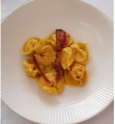 Tortellini con pancetta su piatto bianco.